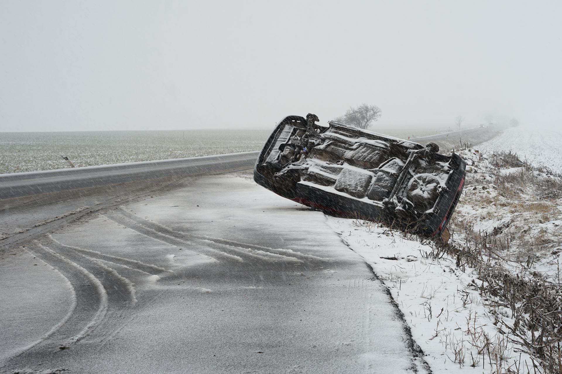 Car flipped on its side on a snow-covered road shoulder, visible tire tracks, overcast sky. Car flipped on its side on a snow-covered road shoulder, visible tire tracks, overcast sky.