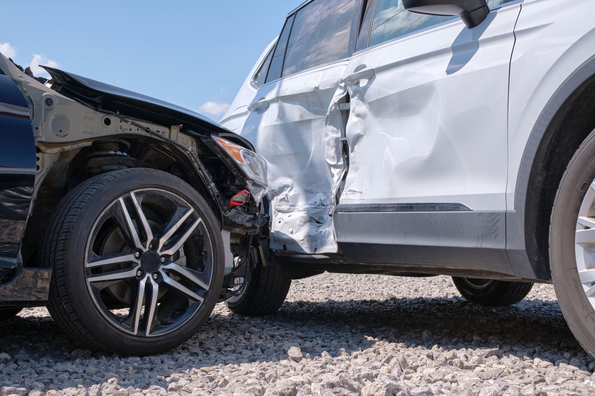 Two cars, a black sedan and a white SUV, are severely damaged in a collision. The white SUV has significant side damage.