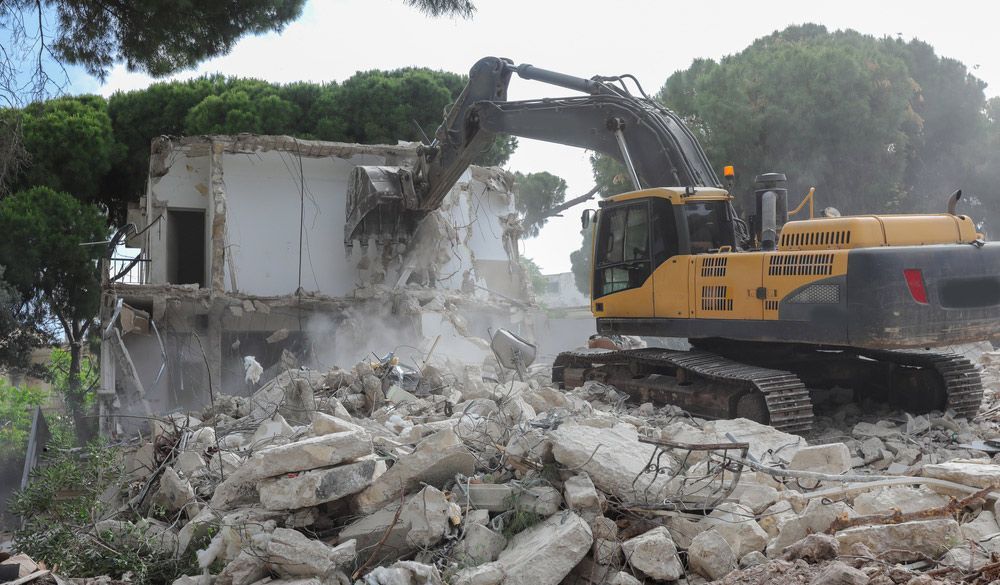 Yellow Excavator is Demolishing a Building With Trees — Boland Contracting in Wellington, NSW