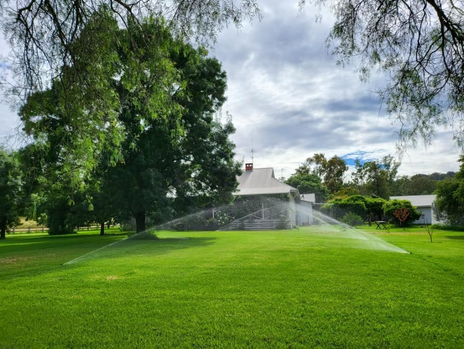 Sprinkler is Spraying Water on a Lush Green Field in Front of a House — Peel Irrigation & Water Supplies in Walcha, NSW