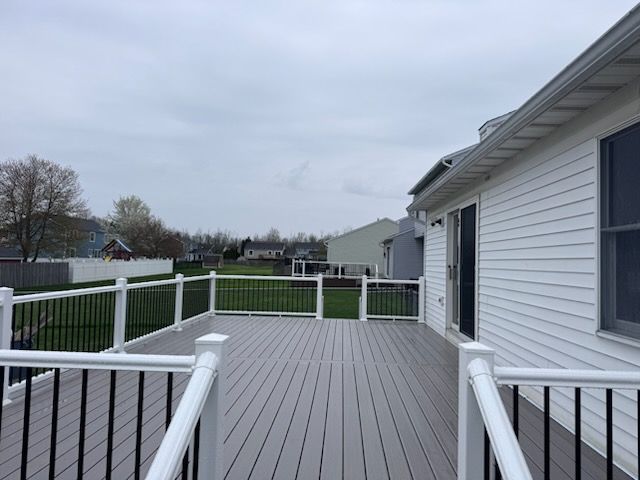 Wooden deck with white railings overlooking a grassy backyard and neighboring houses under a cloudy sky