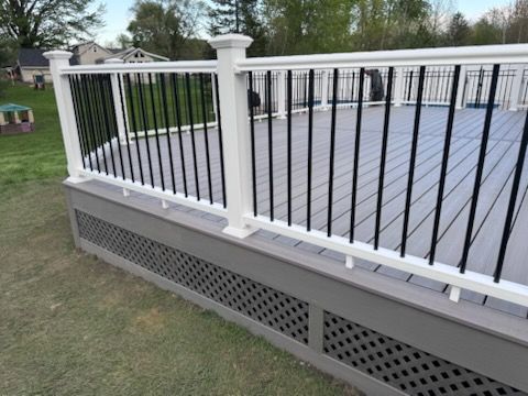 White railing and black balusters around a raised gray deck with a lattice skirt in a grassy yard