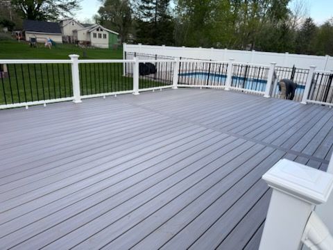 Spacious gray deck with white railing overlooking a green yard and houses.