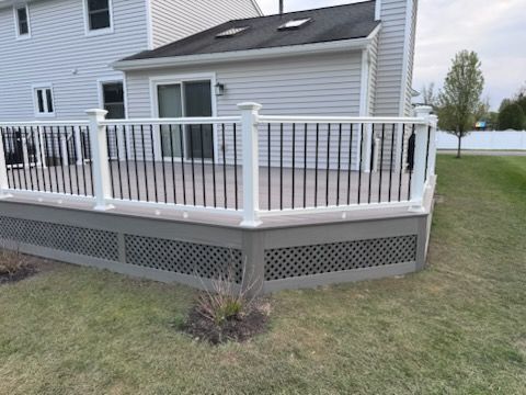 Back deck with white railing and lattice skirting attached to a beige house, overlooking a grassy yard