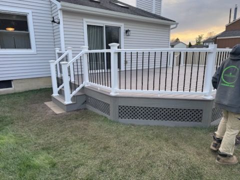 Backyard deck with white railings and gray lattice, beside a house; one person stands at the right edge.