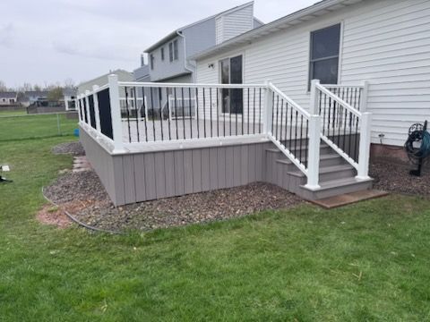Raised white deck with railing and stairs attached to a gray house in a grassy yard
