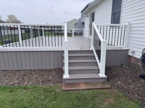 Backyard deck stairs with white railing and gray steps leading to a raised porch