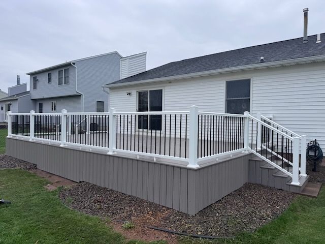 Raised backyard deck with white railing and gray skirting attached to a house.