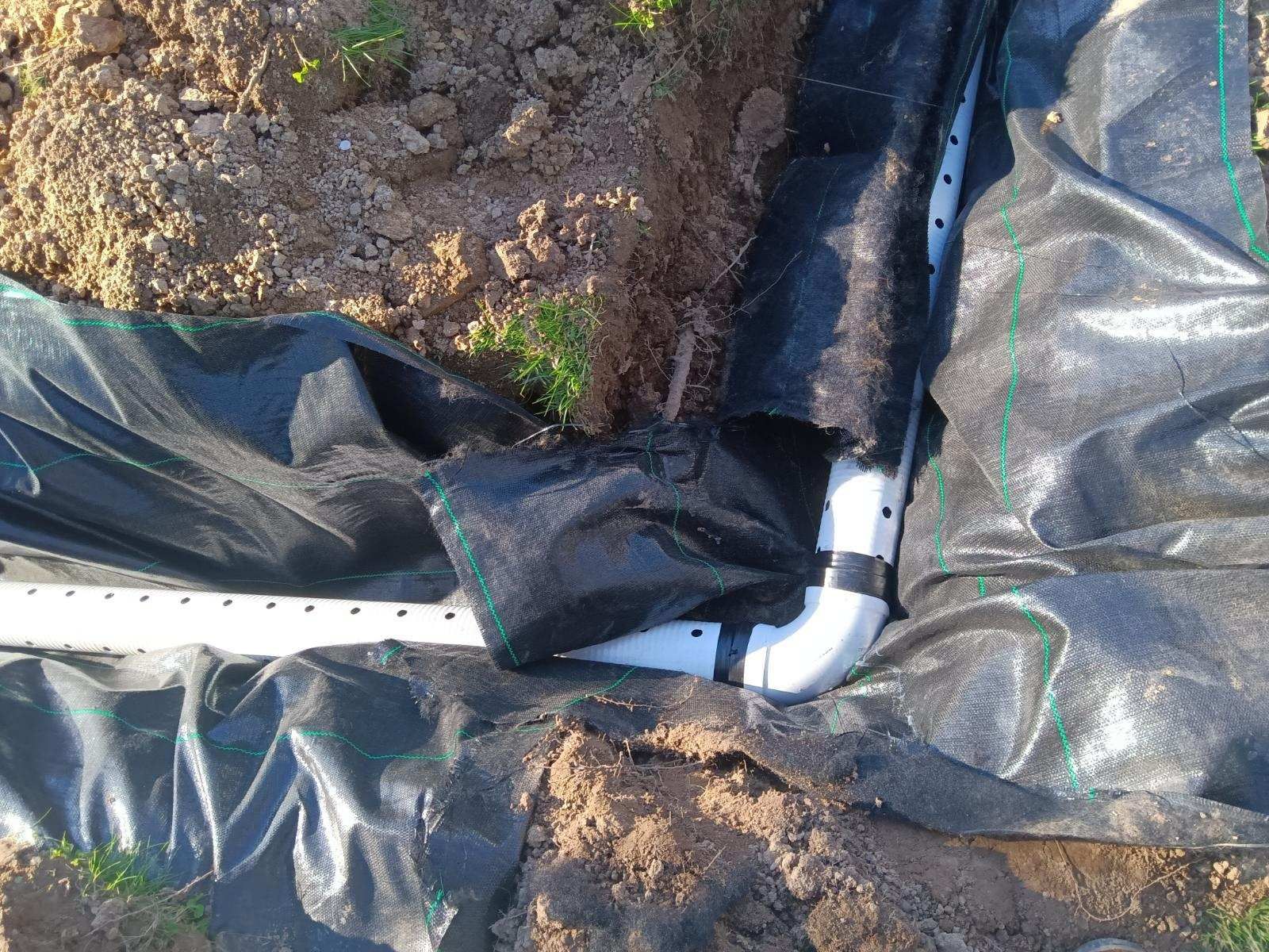 A white pipe is laying in the dirt next to a black tarp.