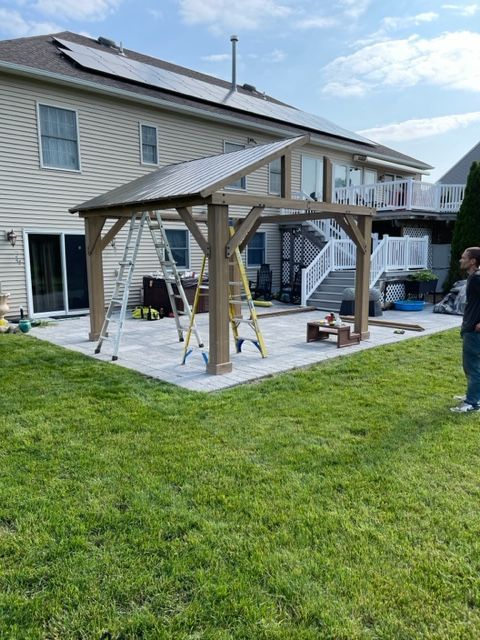 A man is standing in front of a house with a gazebo in the backyard.