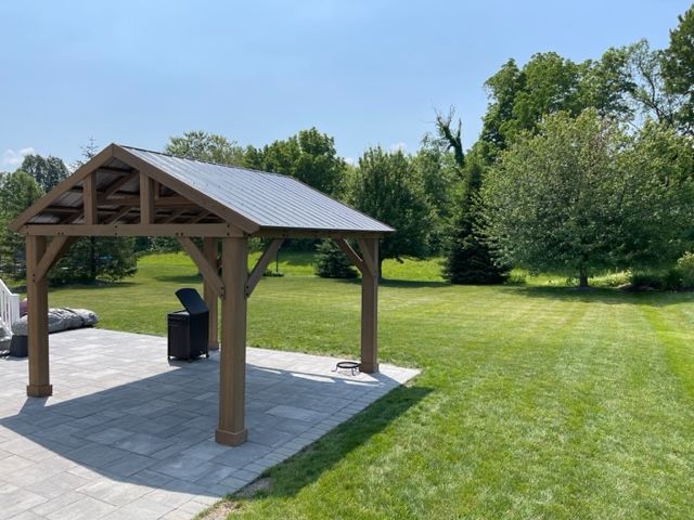 A wooden gazebo with a metal roof is in the middle of a lush green field.