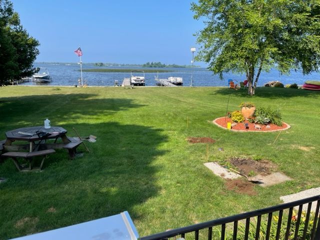 A picnic table is in the middle of a lush green field next to a body of water.