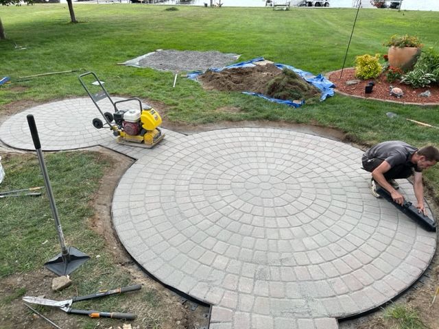 A man is laying bricks in a circle in a yard.