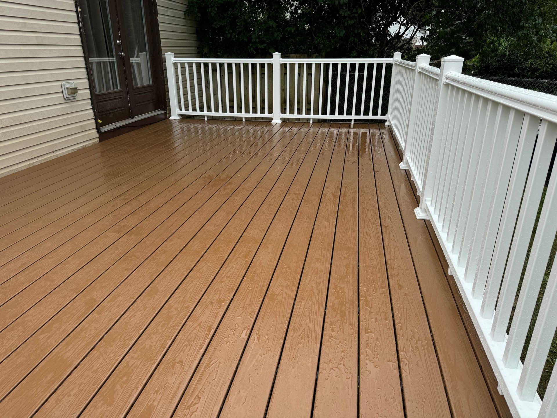 A wooden deck with a white railing and a house in the background.