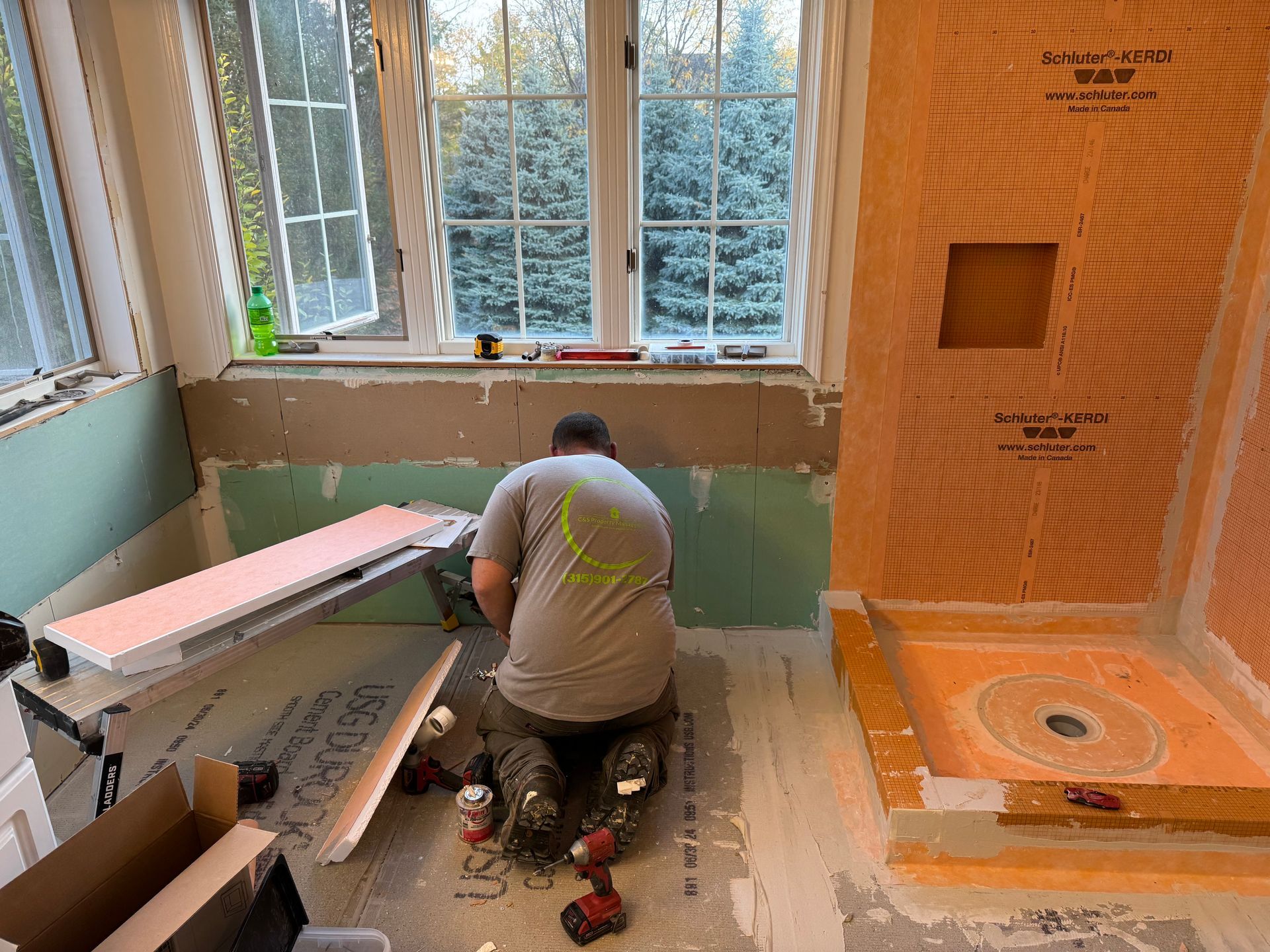 A man is kneeling on the floor in a bathroom under construction.