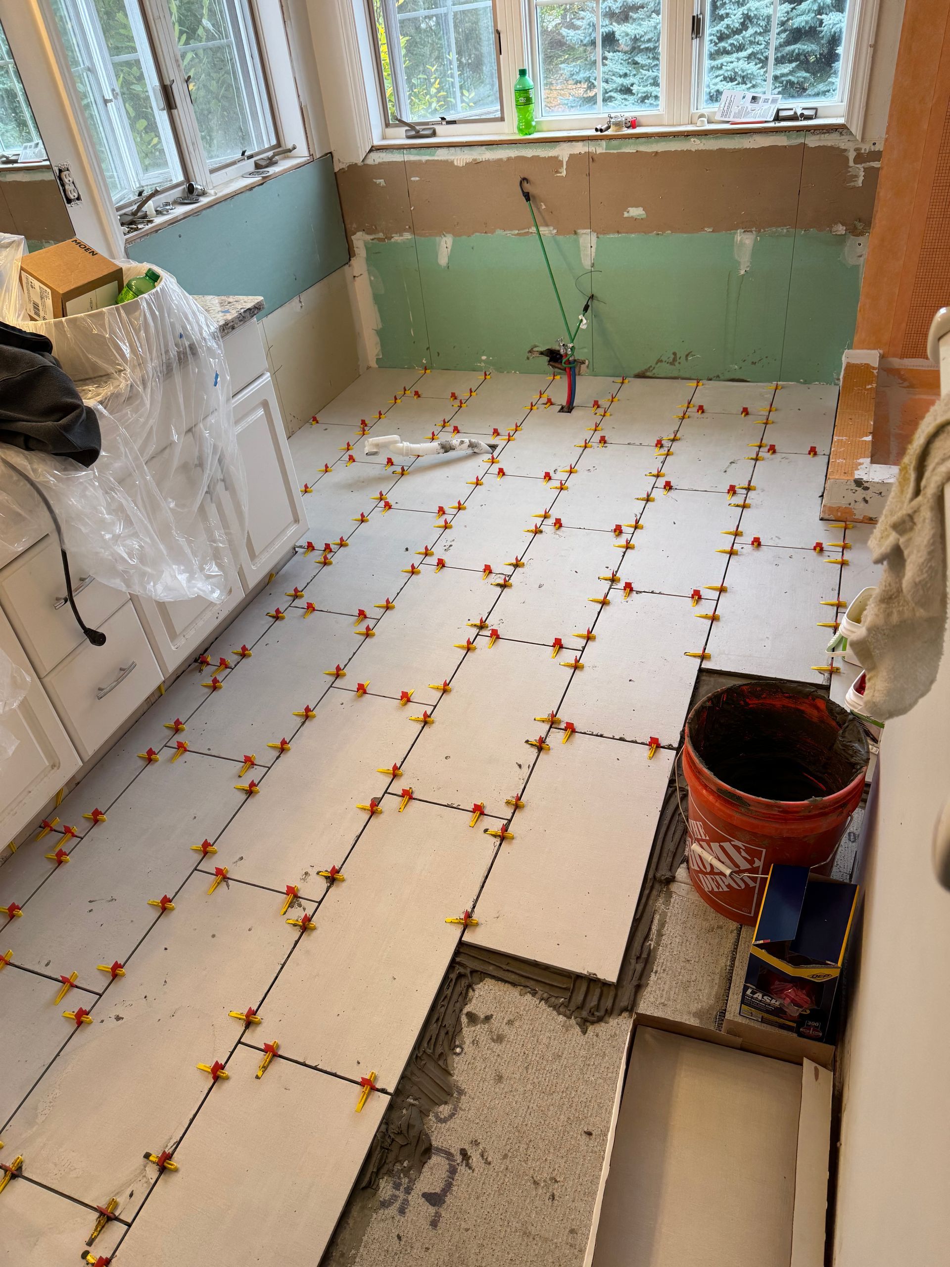 A bathroom floor is being tiled and a bucket of concrete is on the floor.