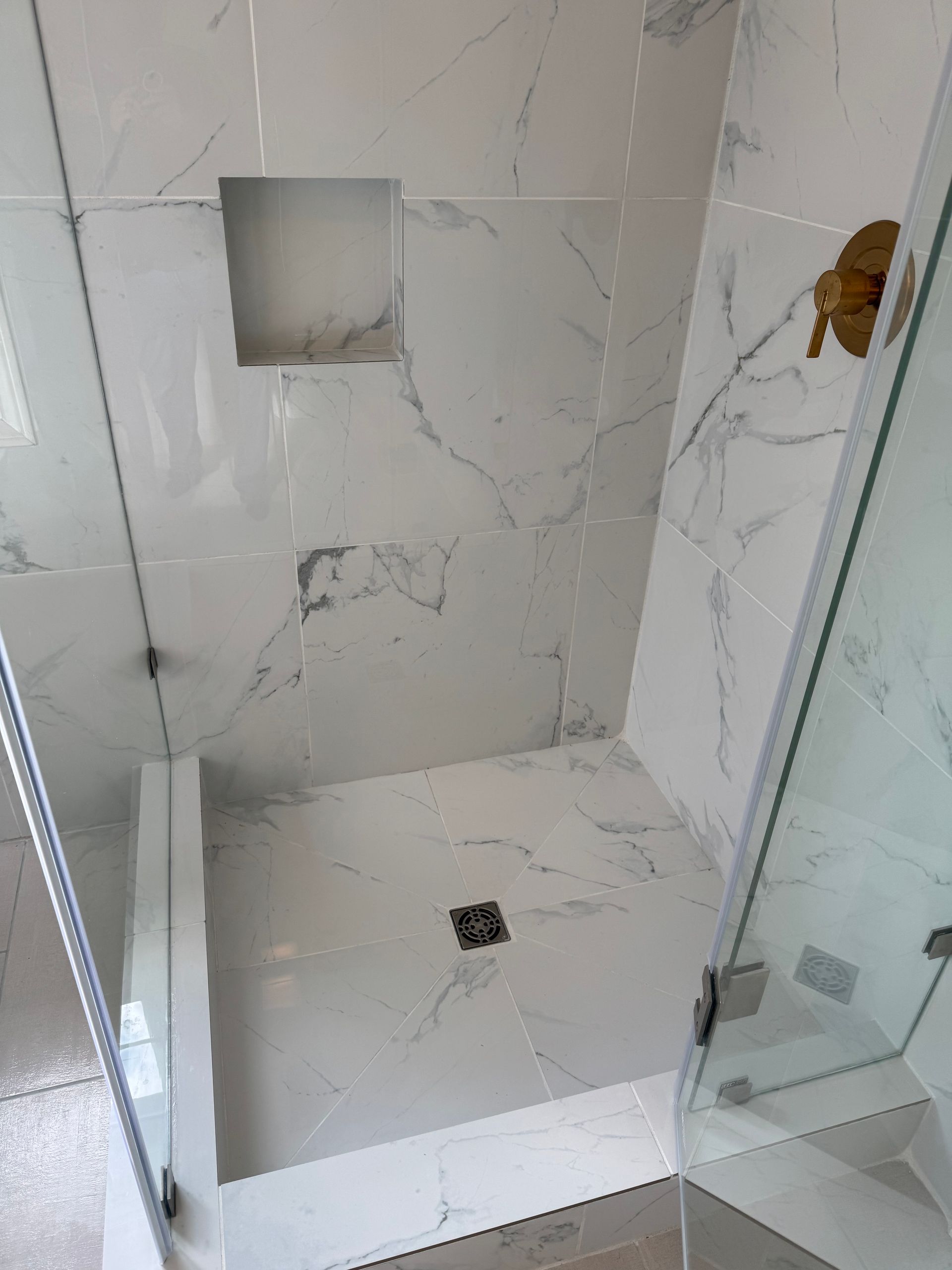 A bathroom with a walk in shower with marble tiles and a glass door.