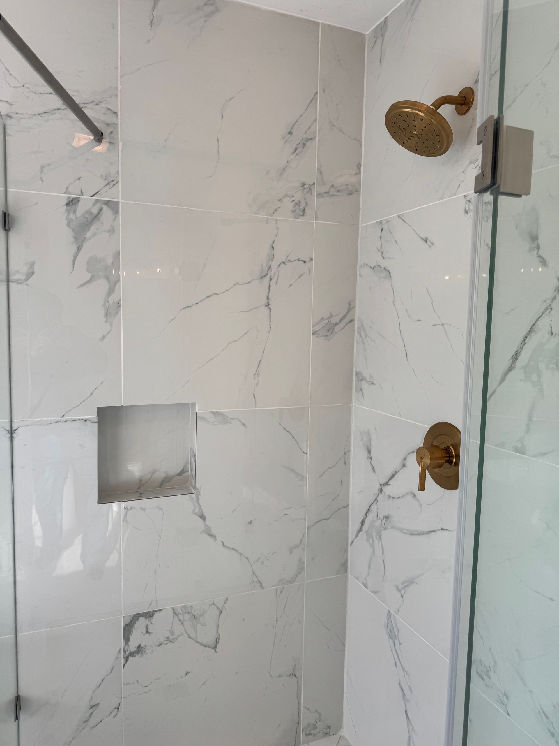 A bathroom with marble tiles and a walk in shower with a gold shower head.