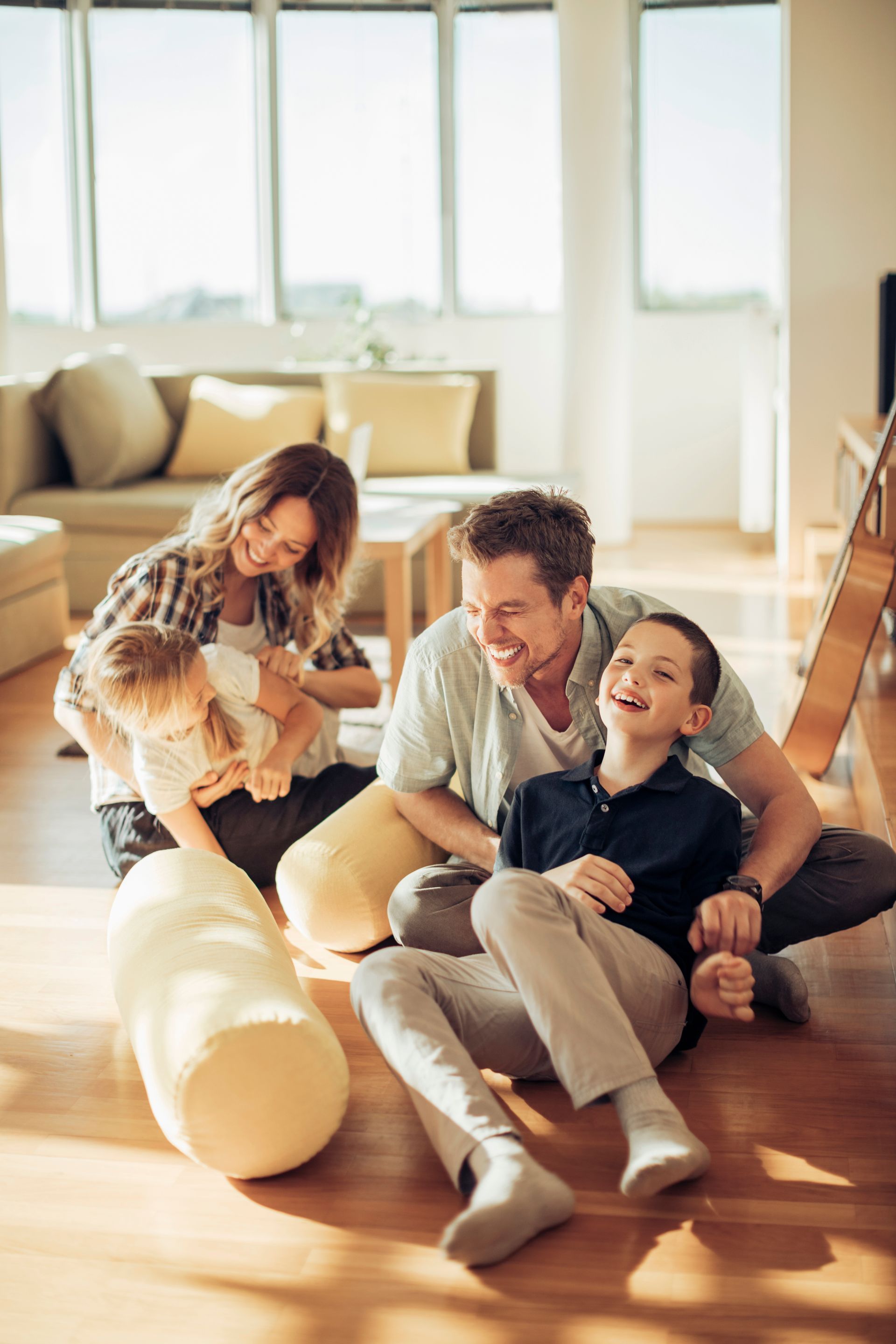 Family laughing together on a hardwood floor in a brightly lit room.