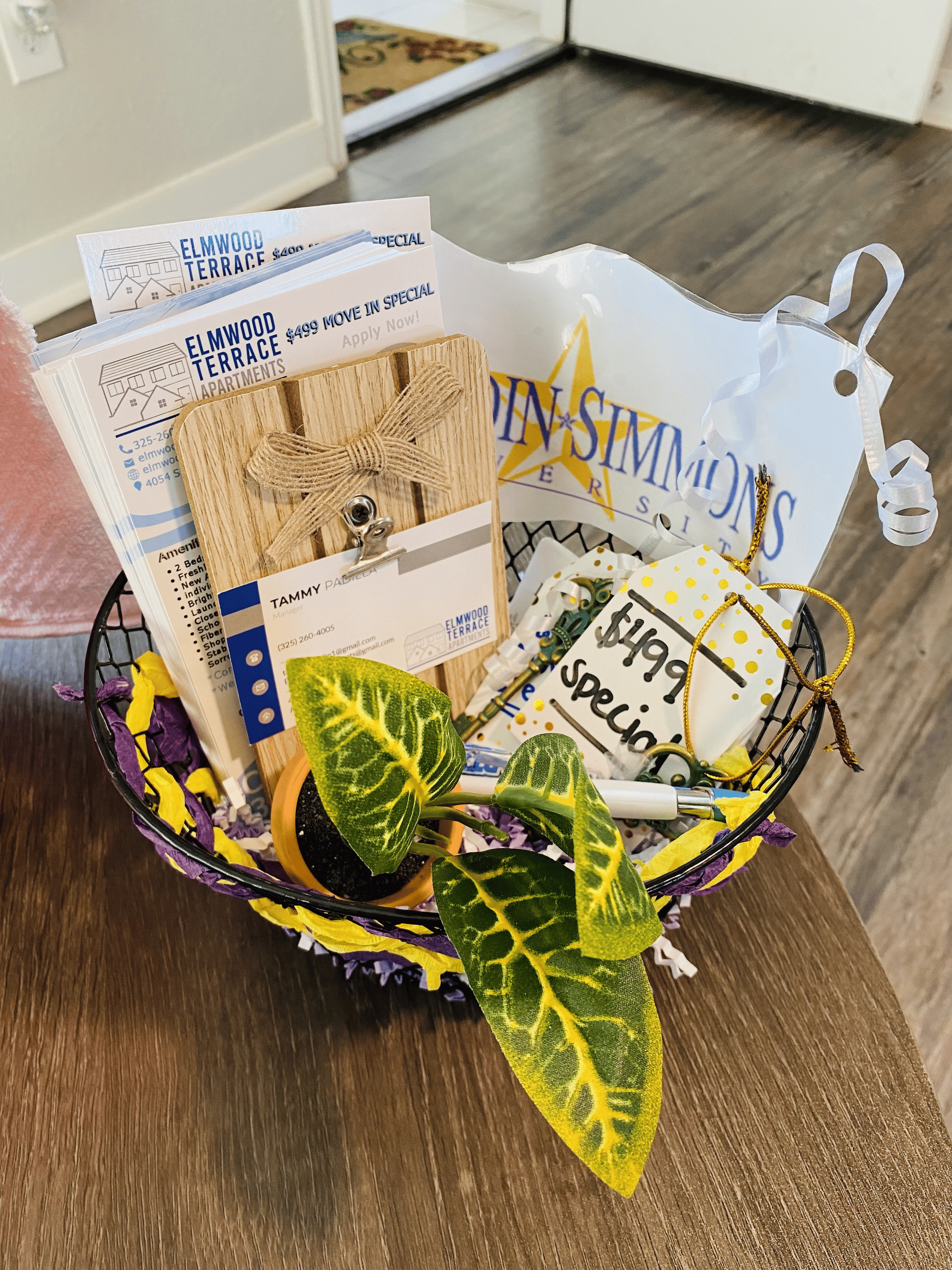 Basket with papers, a wooden plank, plant, and a shopping bag on a wooden surface.
