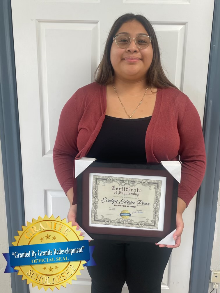 Woman holding framed certificate, smiling in front of a white door; gold seal at the bottom.
