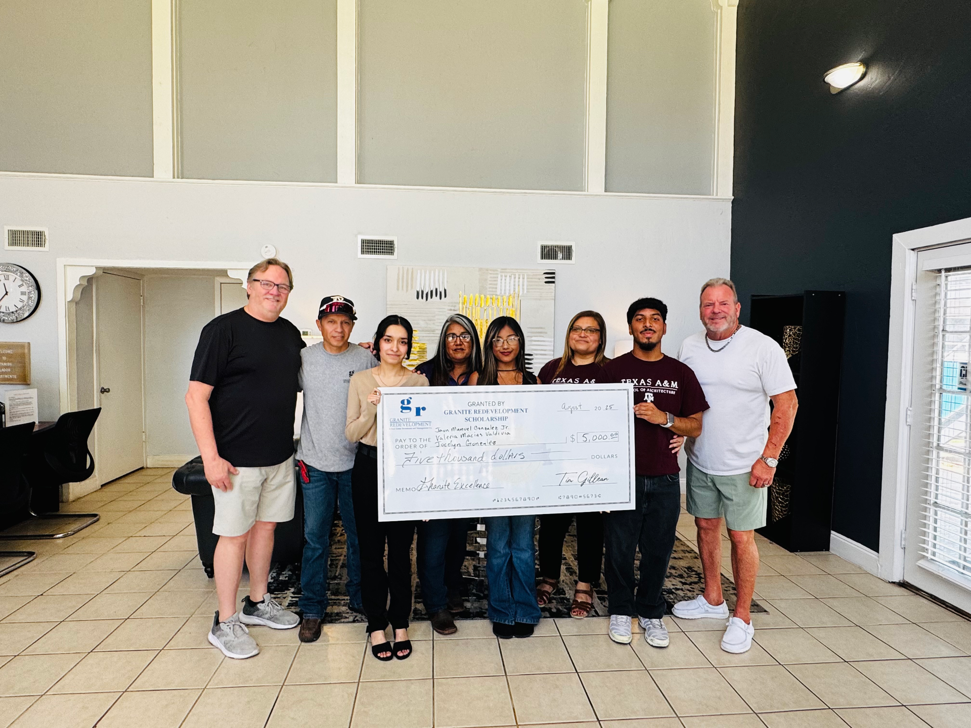 Group of people holding a large check in a light-filled interior.