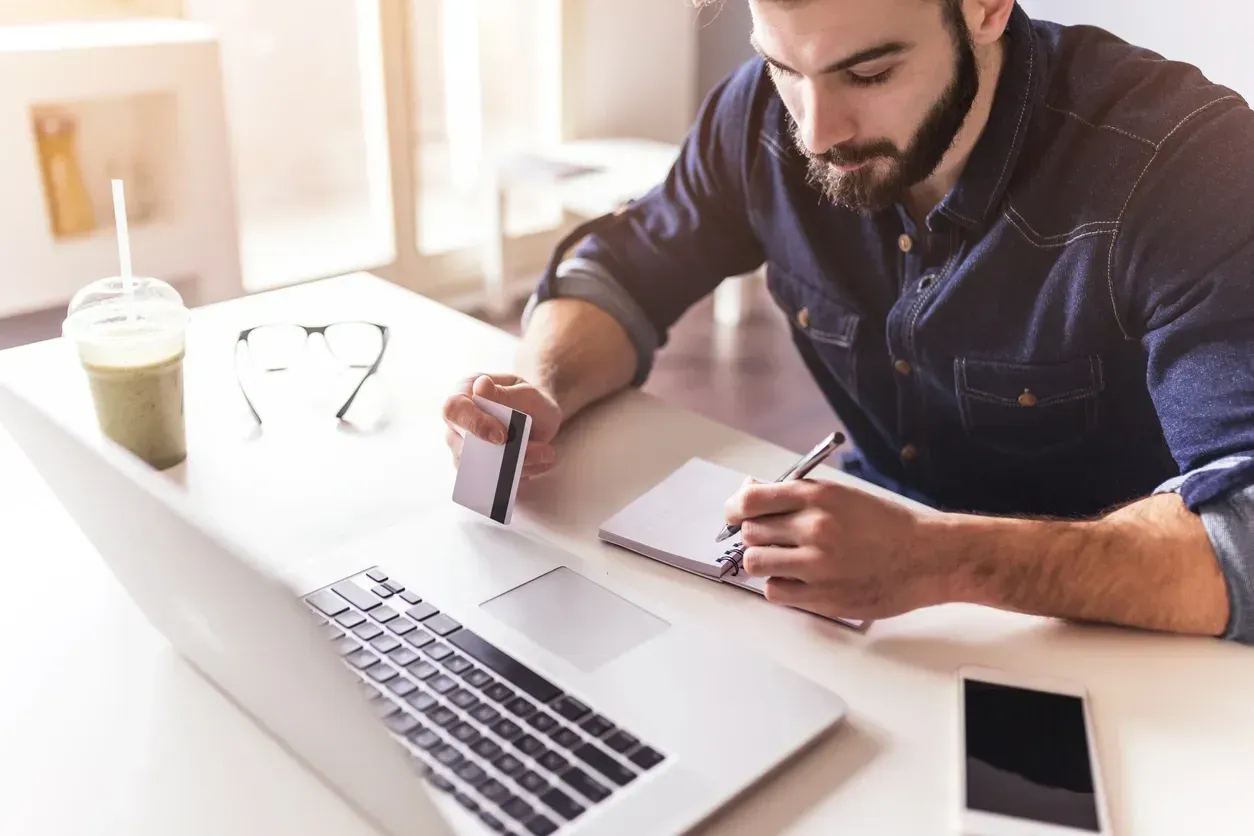 A man is sitting at a desk with a laptop and a credit card.