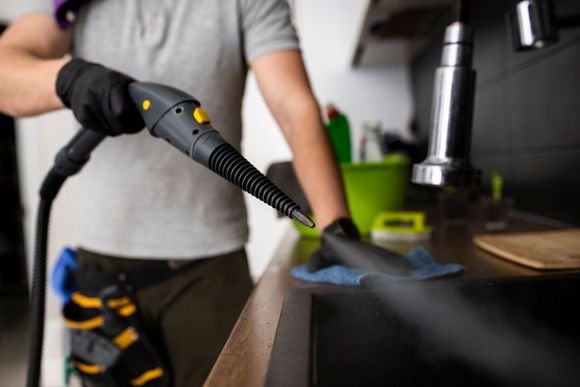 A man is cleaning a kitchen counter with a steam cleaner.