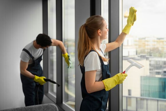 A man and a woman are cleaning a window together.