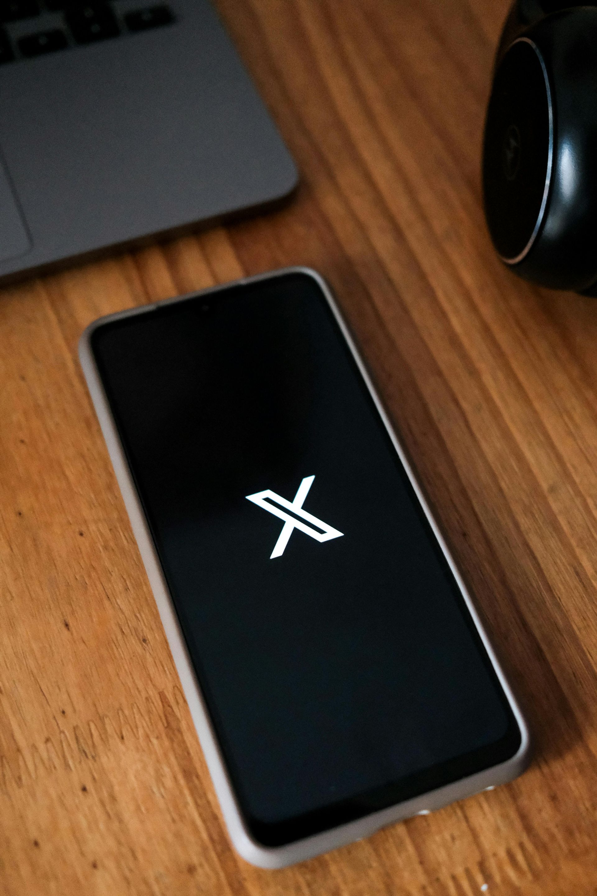A cell phone with the twitter logo on the screen is sitting on a wooden table.