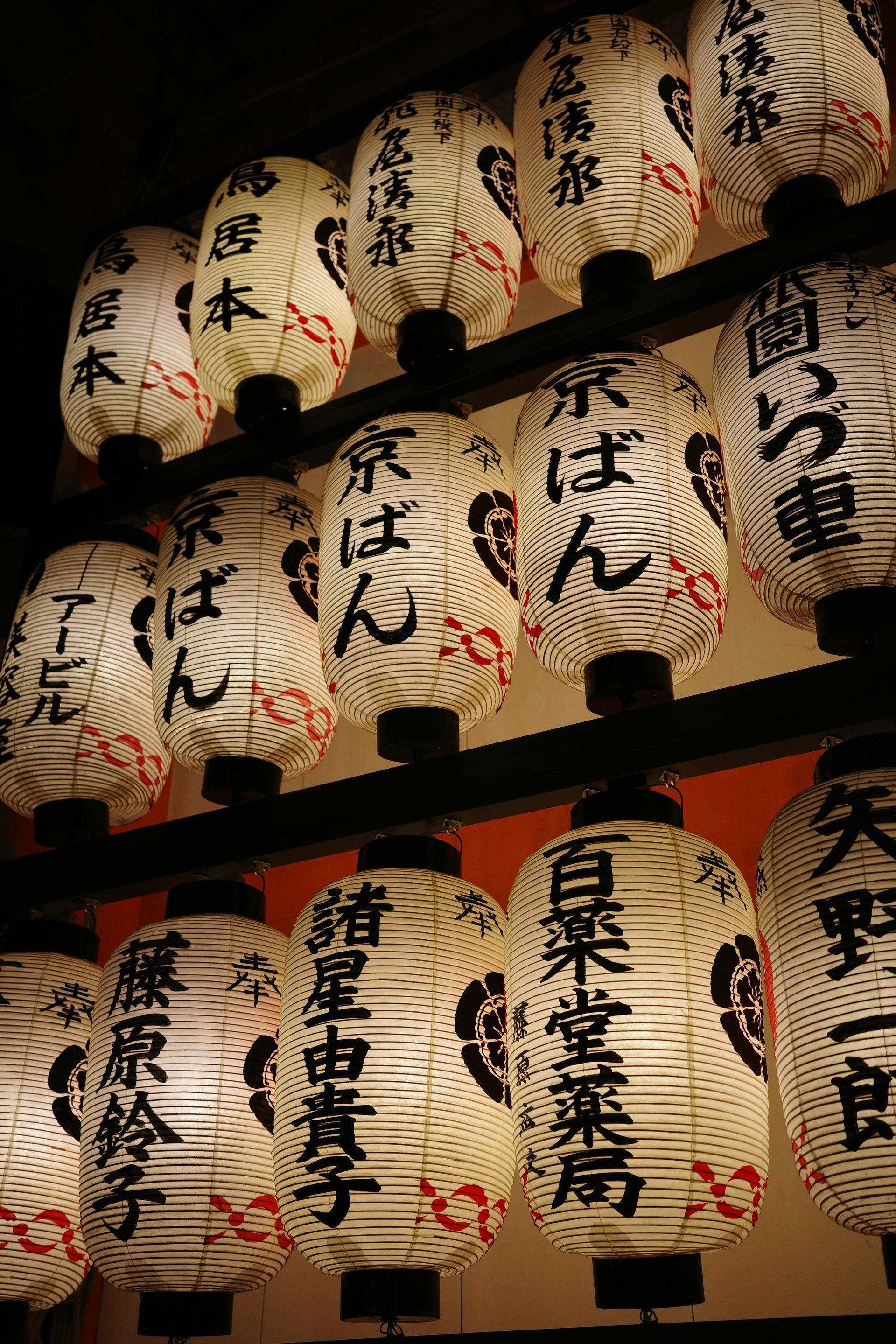 A bunch of lanterns with chinese writing on them are hanging from a ceiling.