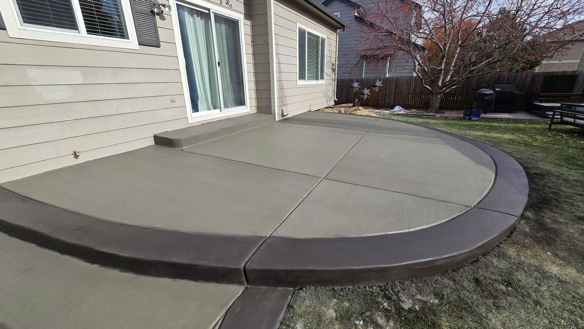 Curved concrete patio beside a house, with a dark border and a narrow walkway leading away.