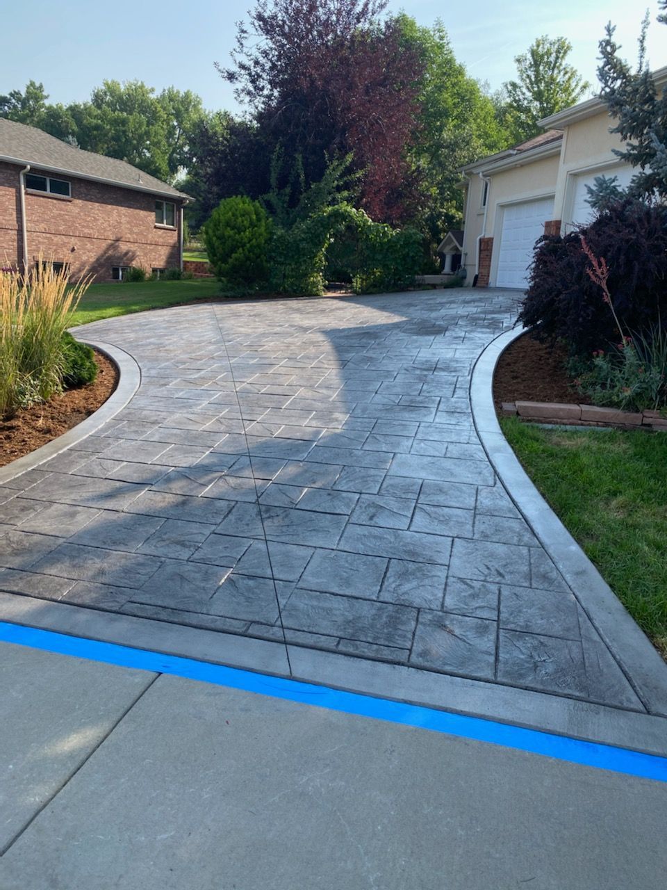 Curved stamped concrete driveway leading to a garage, bordered by landscaping and a blue painted line at the curb