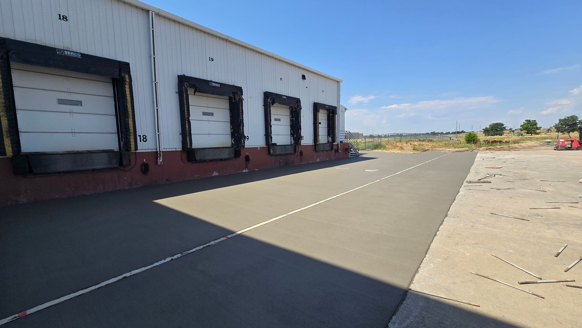 Industrial warehouse loading dock with closed bay doors beside a wide concrete lot under a clear sky