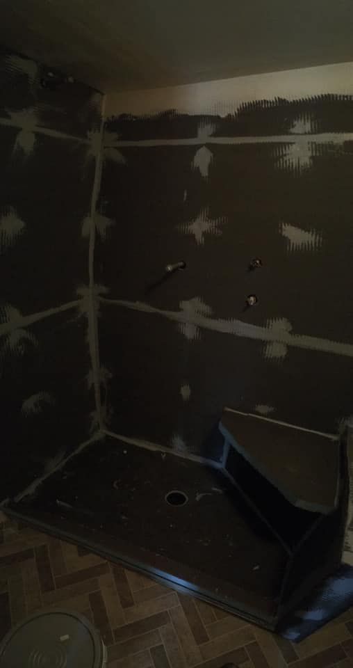 Black shower with unfinished walls, plumbing fixtures, and a corner seat, being built inside.