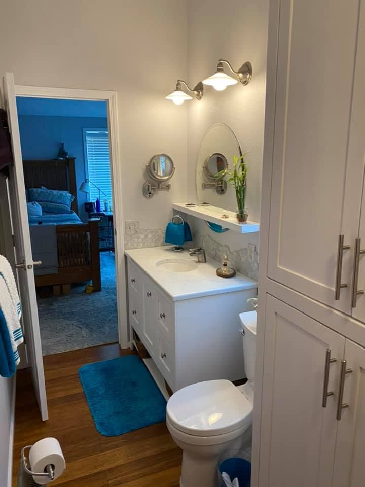 Bathroom with white cabinets, toilet, and sink. A doorway leads to a bedroom.