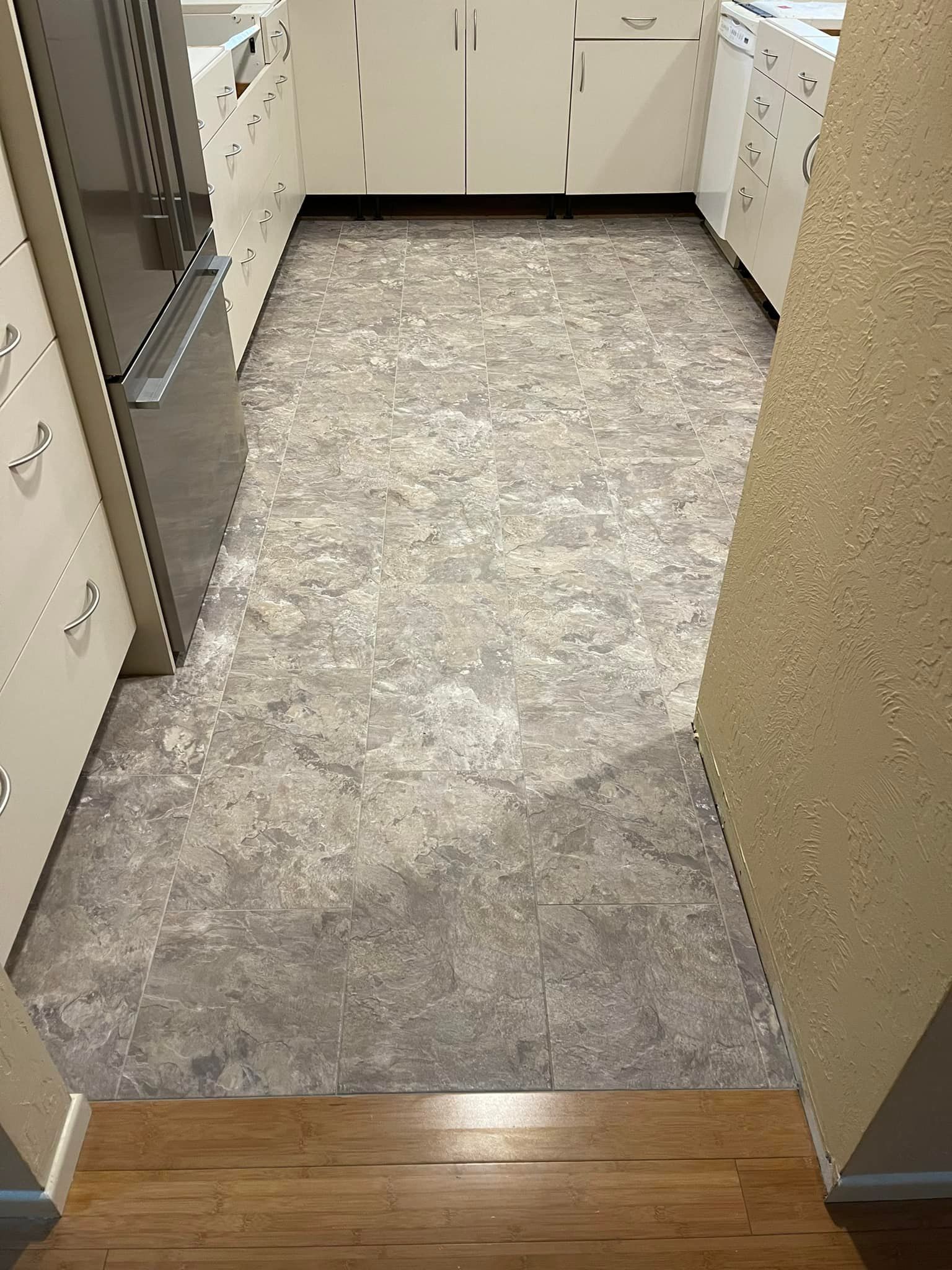 Kitchen with gray patterned floor, white cabinets, and a doorway with wooden flooring.