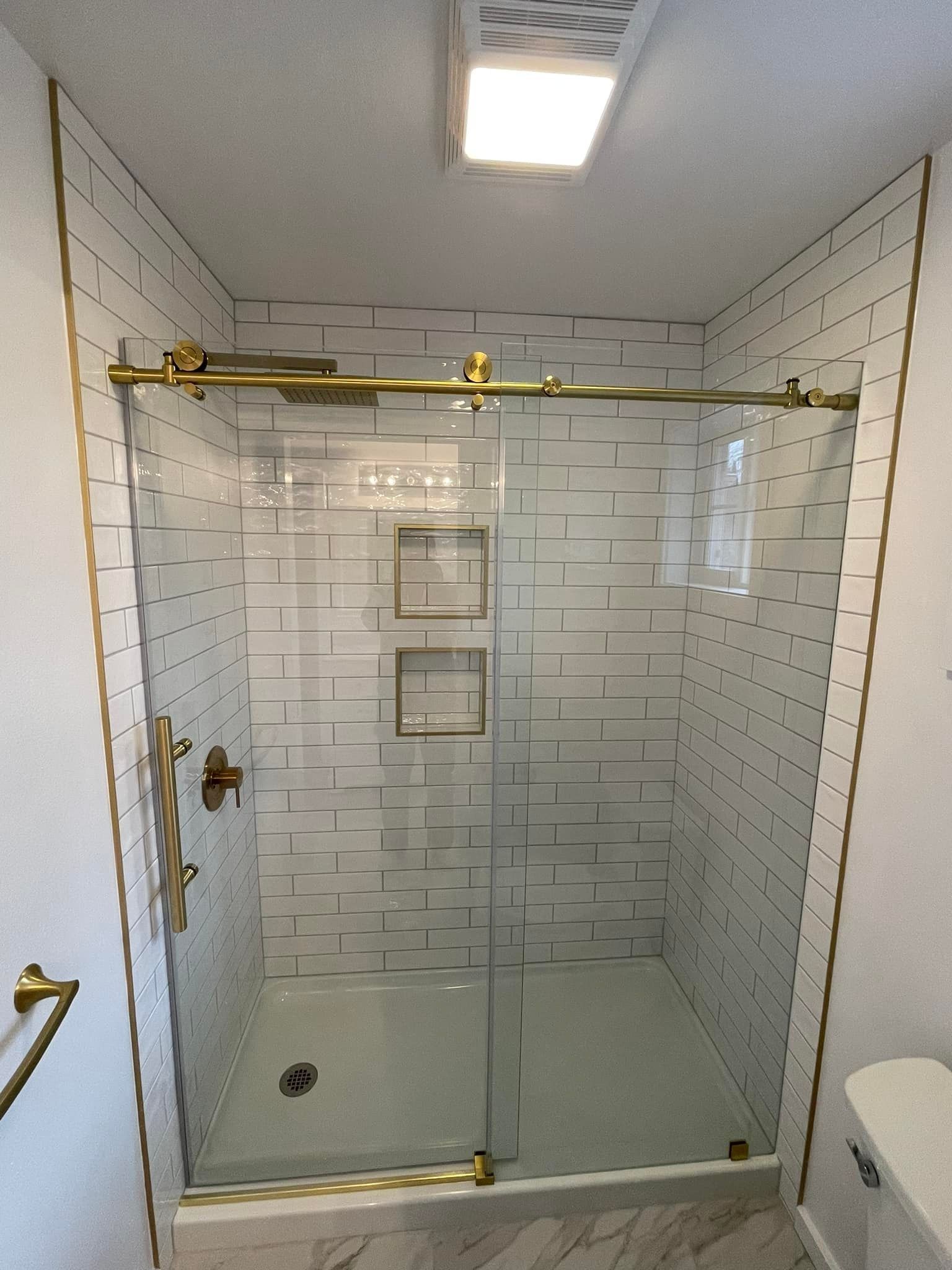 Modern bathroom with glass shower doors and gold fixtures; white tile walls.
