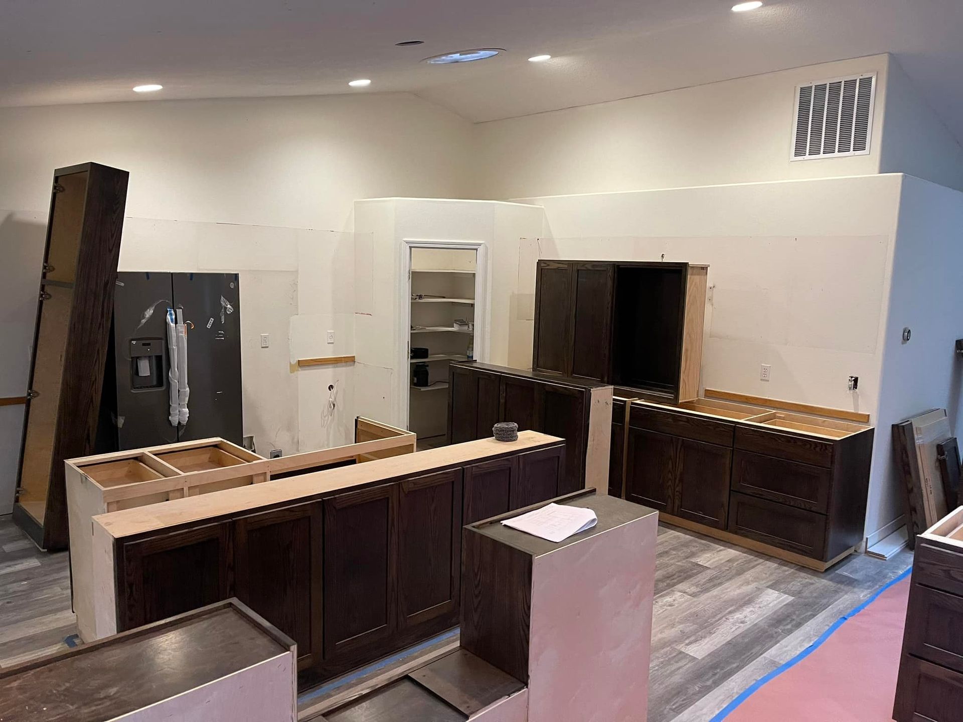 Kitchen remodel in progress, dark cabinets installed on white walls, appliance and unfinished cabinets.