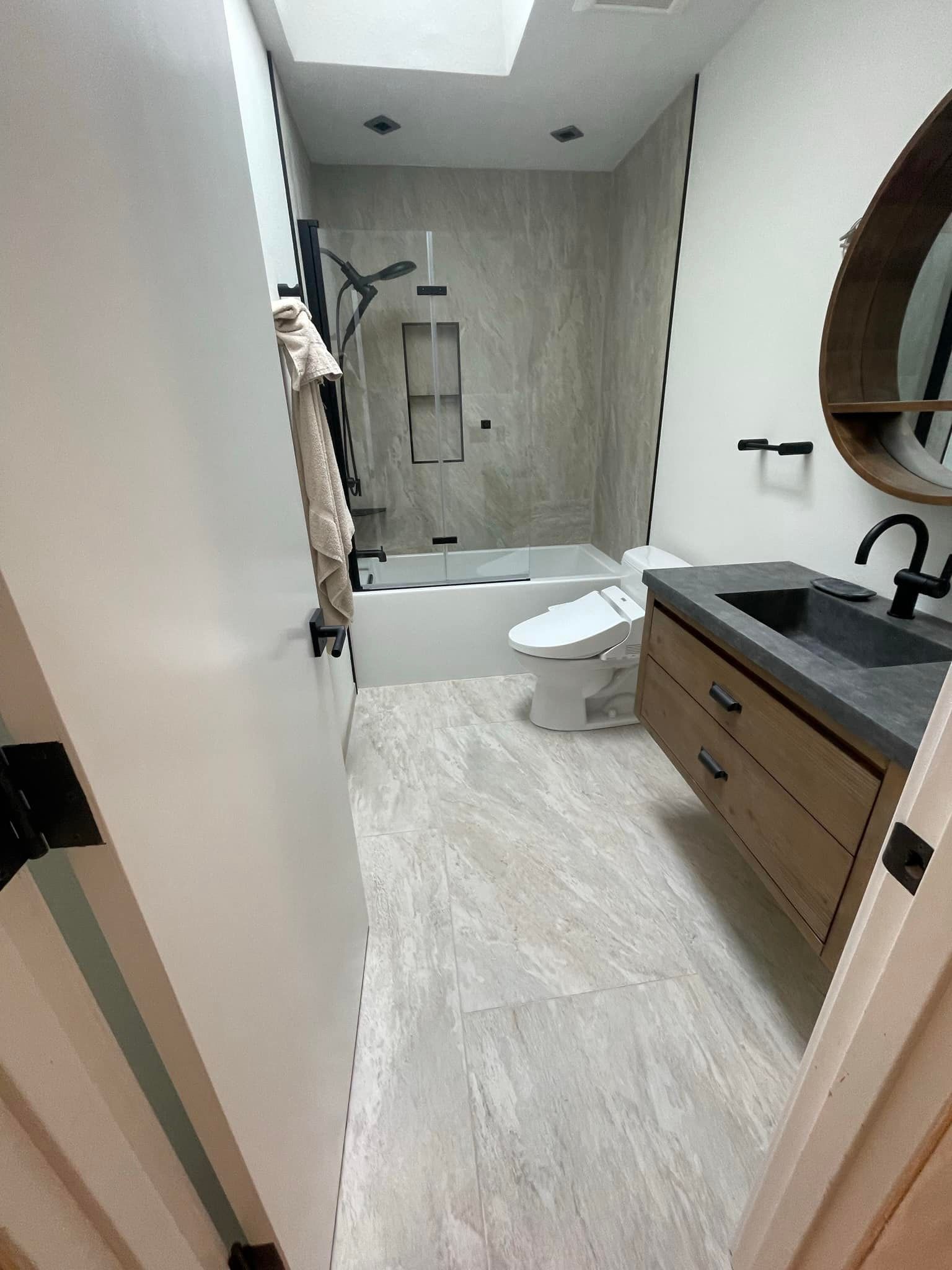 Bathroom with light gray tiled floor, a shower, a toilet, a vanity with a dark countertop and a wood cabinet.