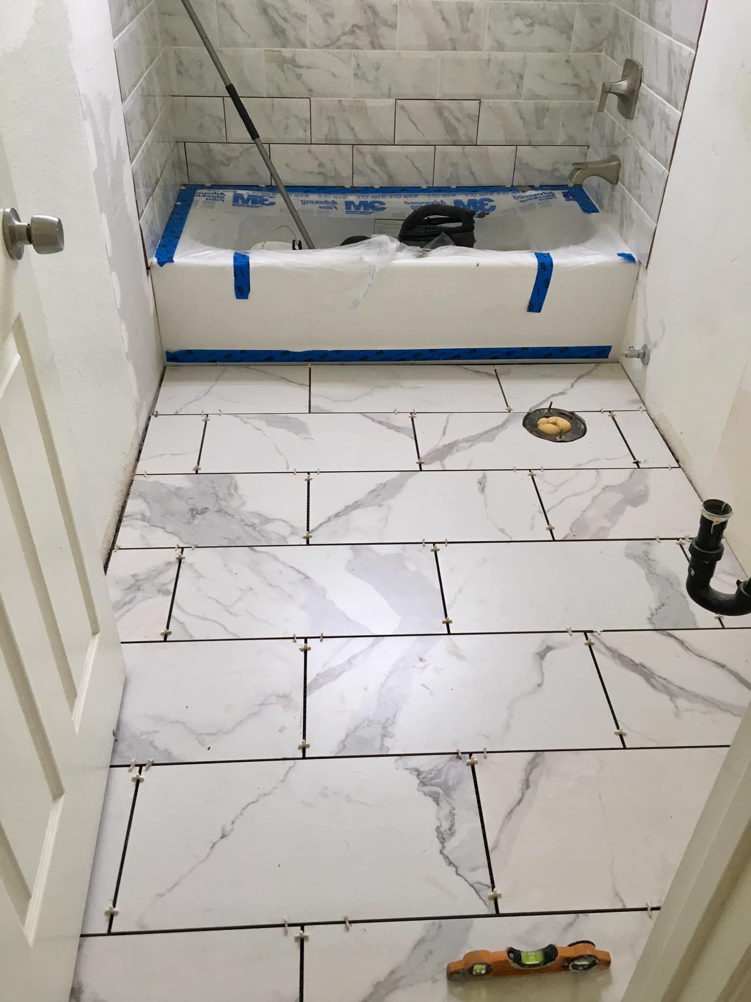 Bathroom with white marble-look tiles on the floor and walls, bathtub, and door. Construction in progress.