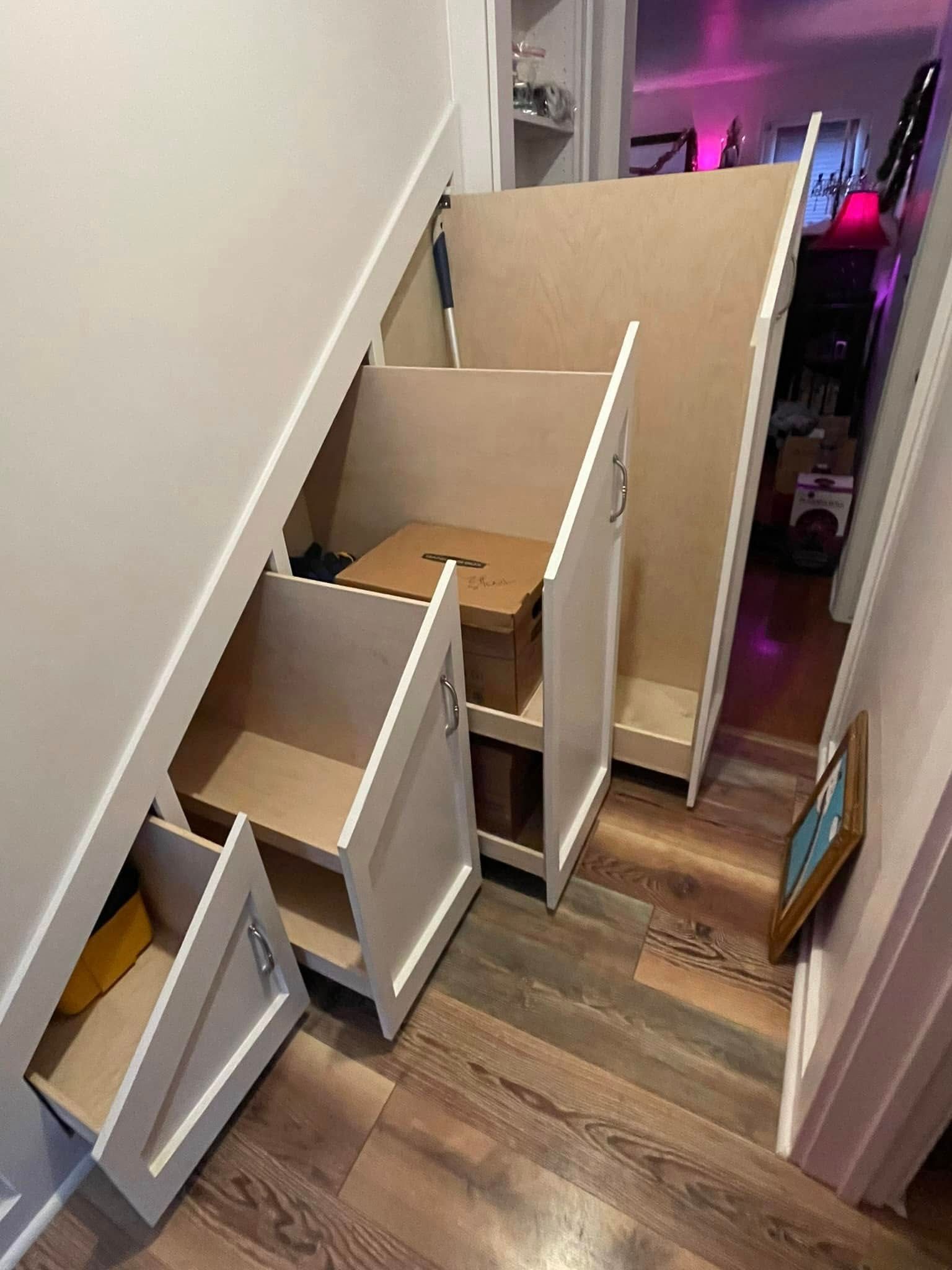 Staircase with built-in storage drawers, painted white. Brown laminate flooring. The storage units are open.