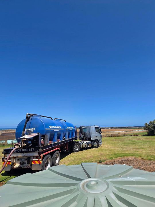 Blue tanker truck parked in a grassy field under a clear blue sky