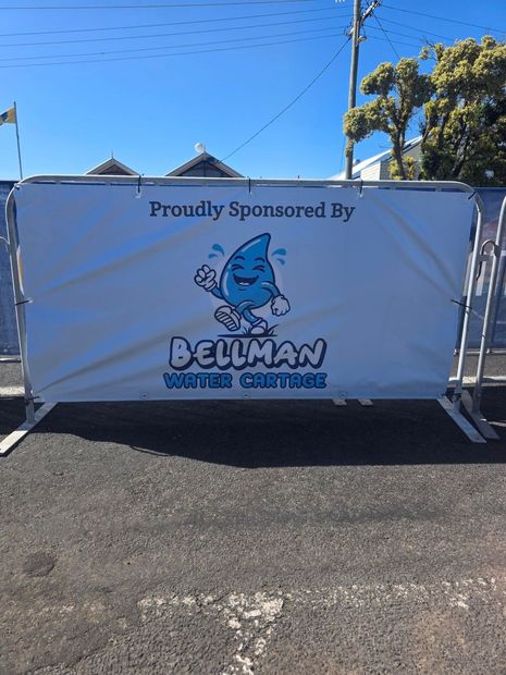 Event sponsor banner for Bellman Water Services on a white fence outdoors under a clear blue sky