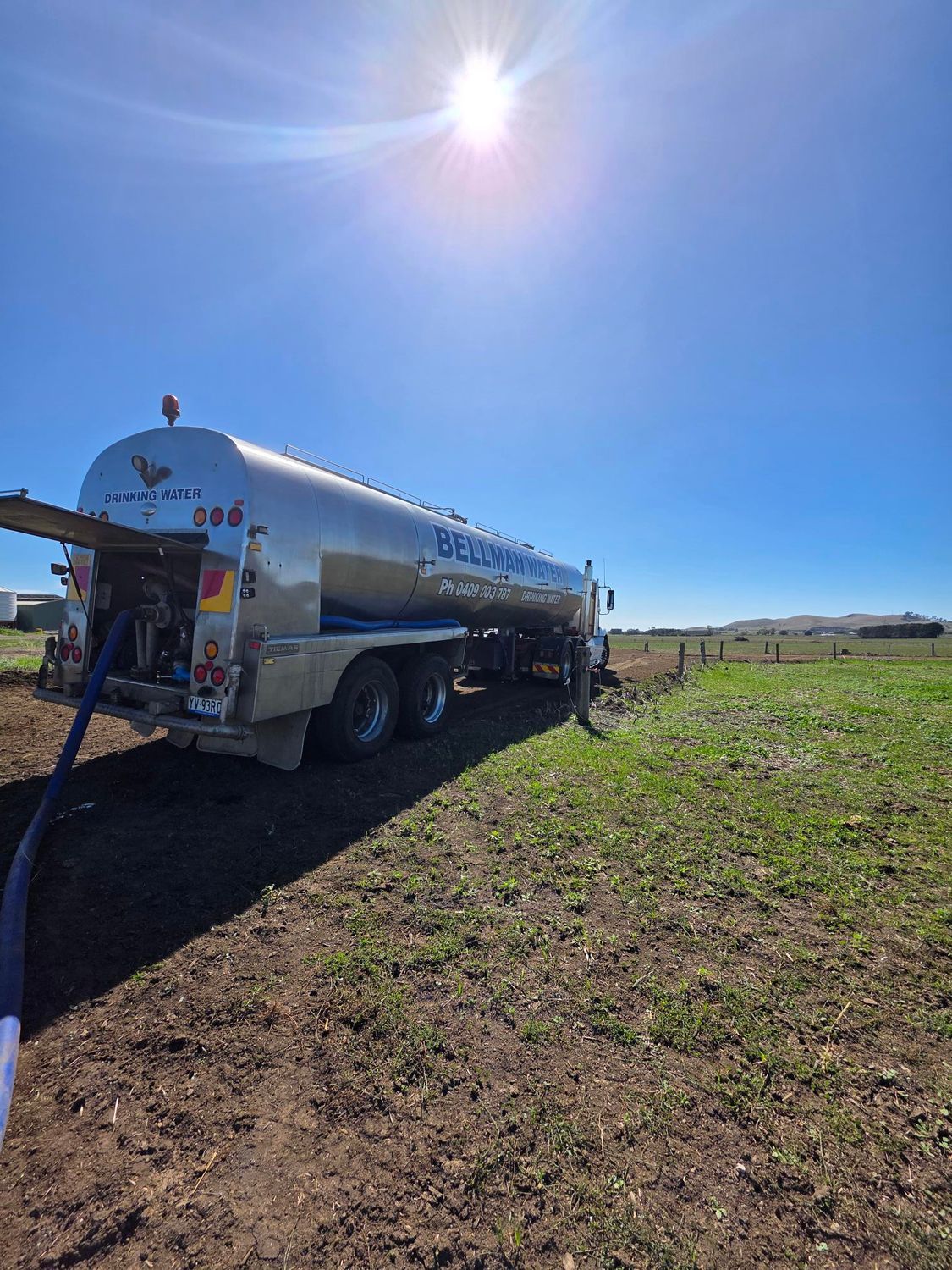 Fuel tanker truck parked in a sunny field, with a person working at the rear hatch.