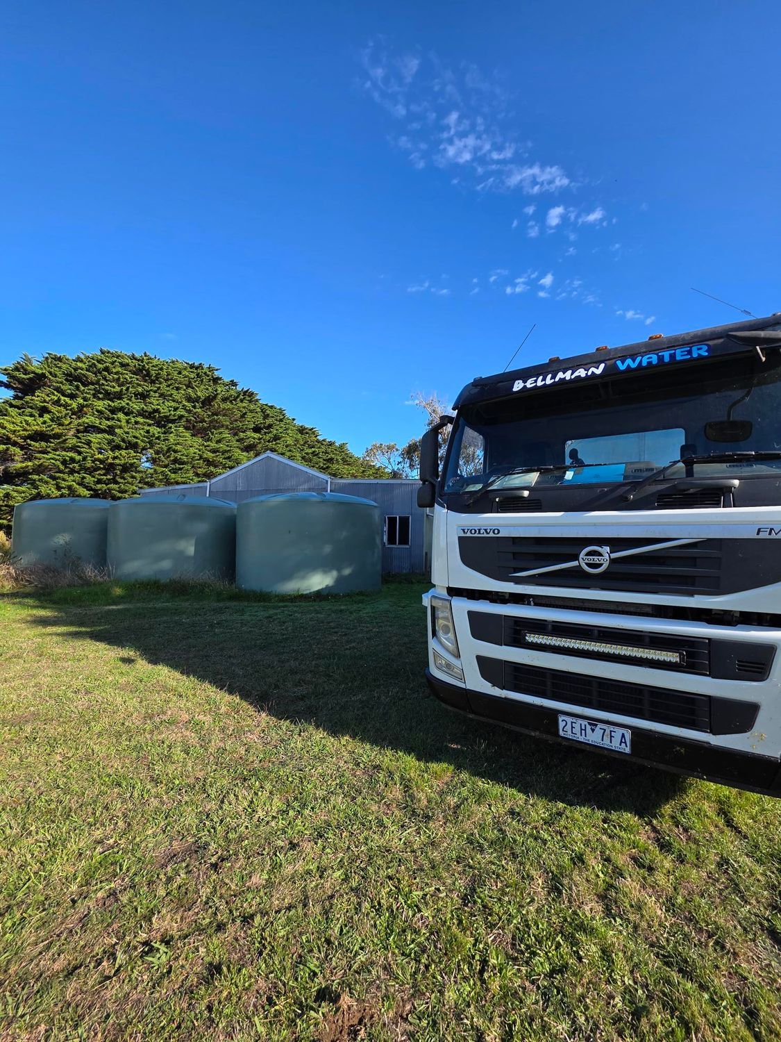 White Volvo truck parked on grass beside green tents under a clear blue sky