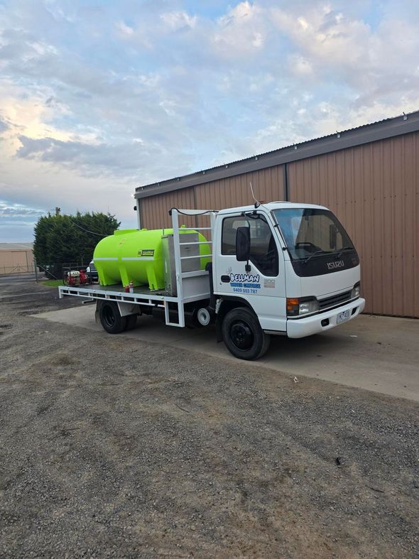 Small white utility truck with a bright green tank parked on a gravel lot under a cloudy sky