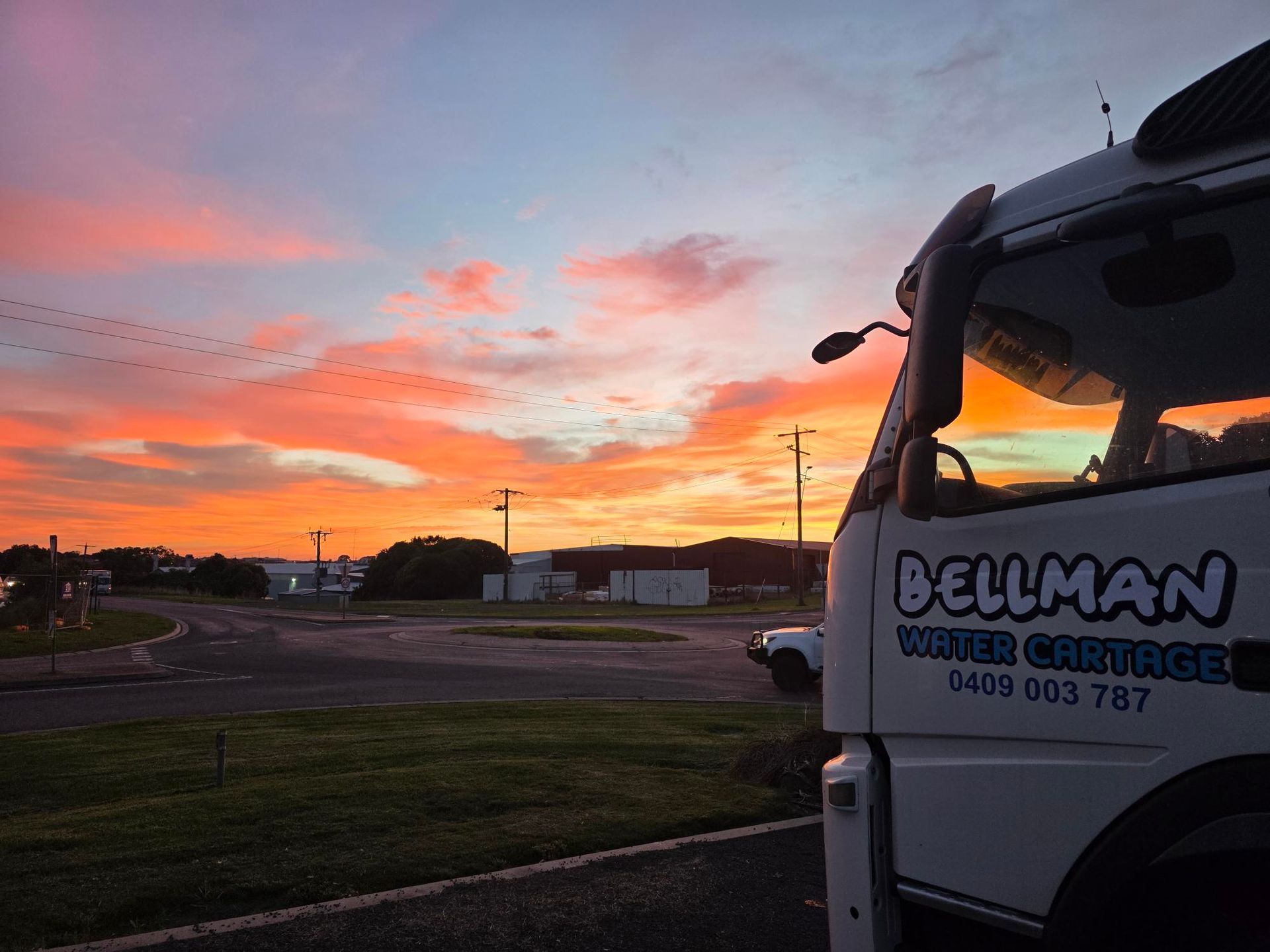 Trucking yard at sunset, with a Bellman truck in the foreground and orange-pink sky behind.