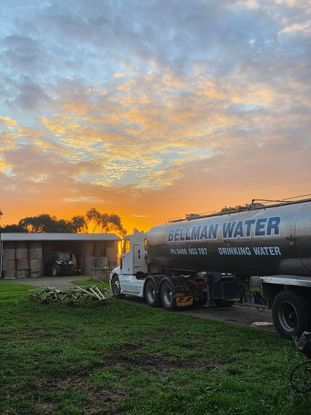 Water tanker truck parked by a house at sunset under a colorful sky