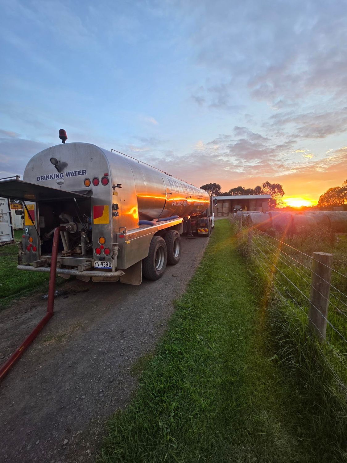 Silver trailer on gravel path at sunset, with warm lights glowing beside a grassy field.
